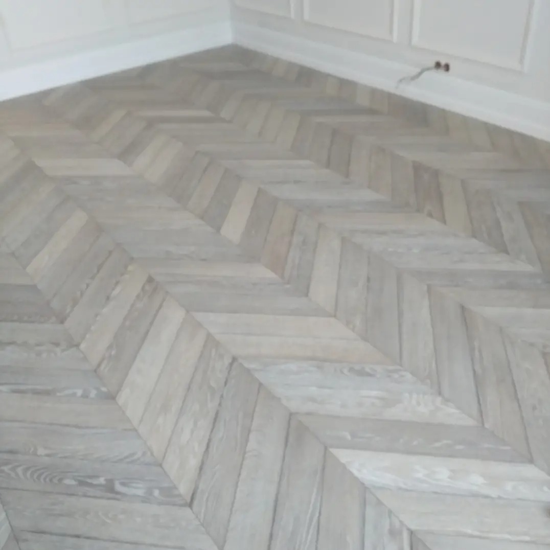 Jasnoszara podłoga ułożona w jodełkę francuską, widok z góry. Eleganckie wykończenie wnętrza z listwami przypodłogowymi. Minimalistyczny design.