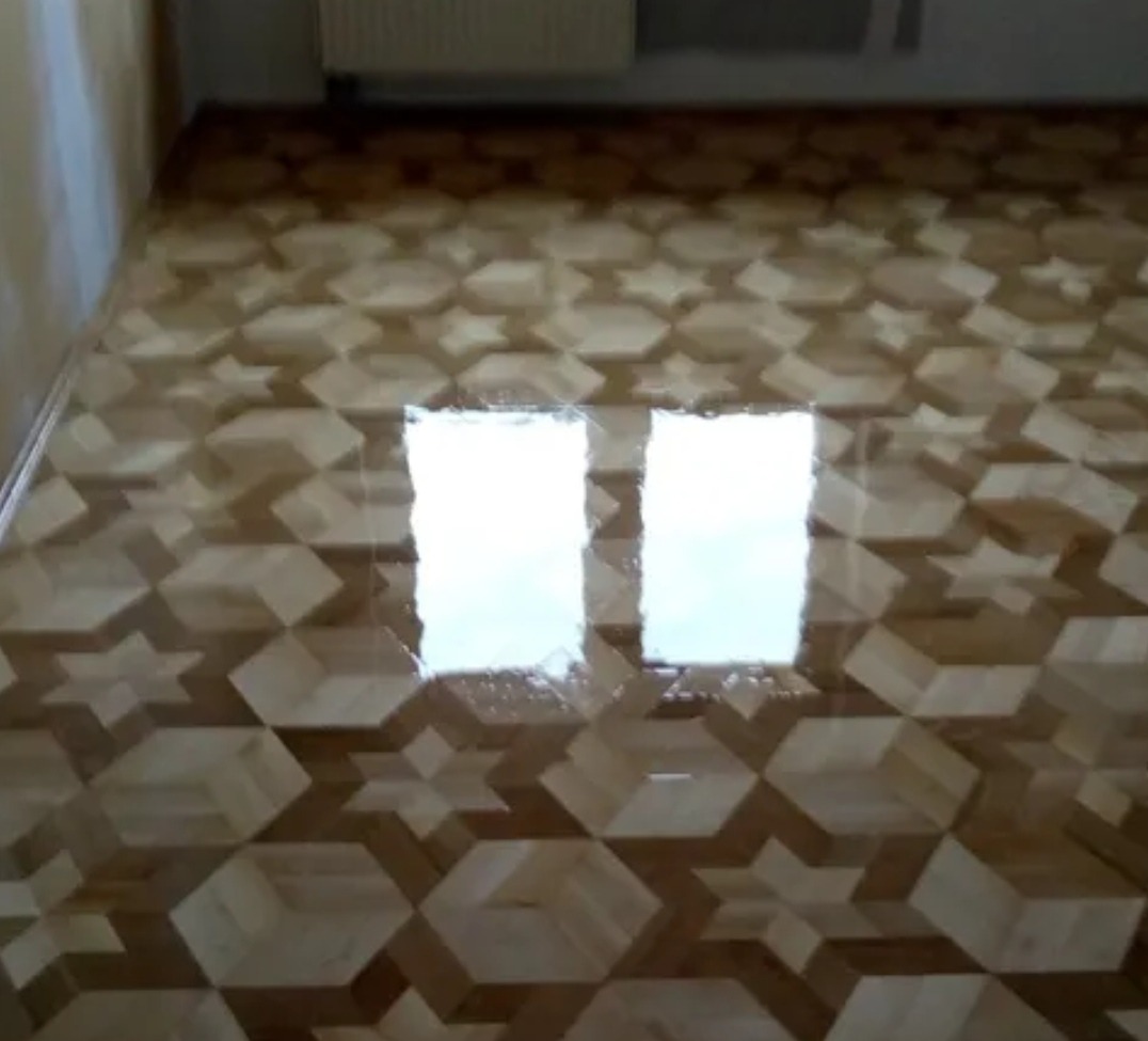 Błyszcząca, nowa podłoga z parkietu w geometryczny wzór gwiazd i sześcianów, odbijająca światło okna. Jasne drewno, świeżo po lakierowaniu.