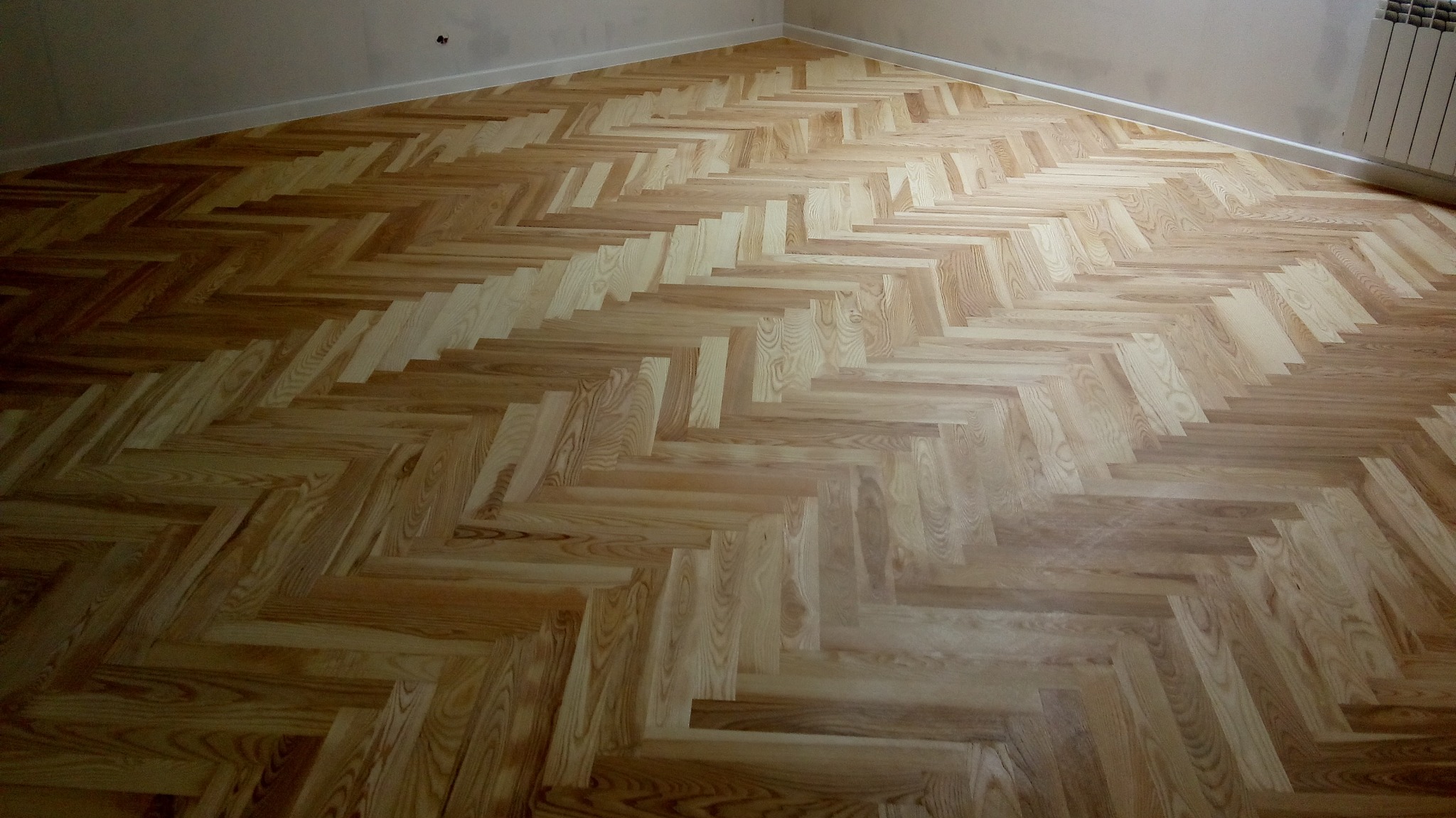 Jasny parkiet ułożony we wzór jodełki francuskiej, widok z góry, świeżo po ułożeniu, z widocznymi detalami słojów drewna i subtelnym połyskiem.