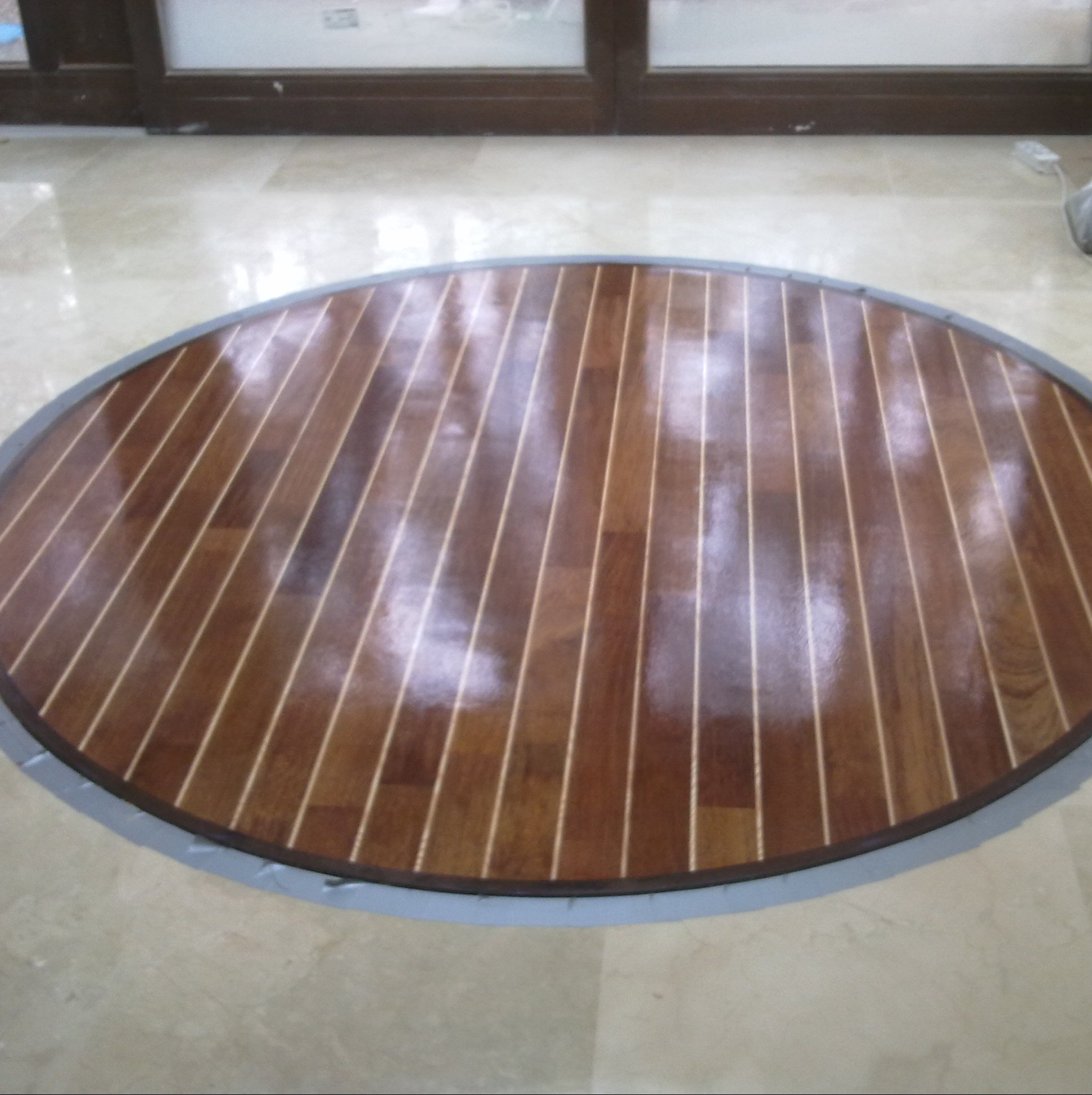 Okrągła intarsja parkietowa z ciemnego drewna, ułożona na jasnej marmurowej posadzce. Dekoracyjny element podłogi w stylu marynistycznym, z wyraźnymi liniami spoin.