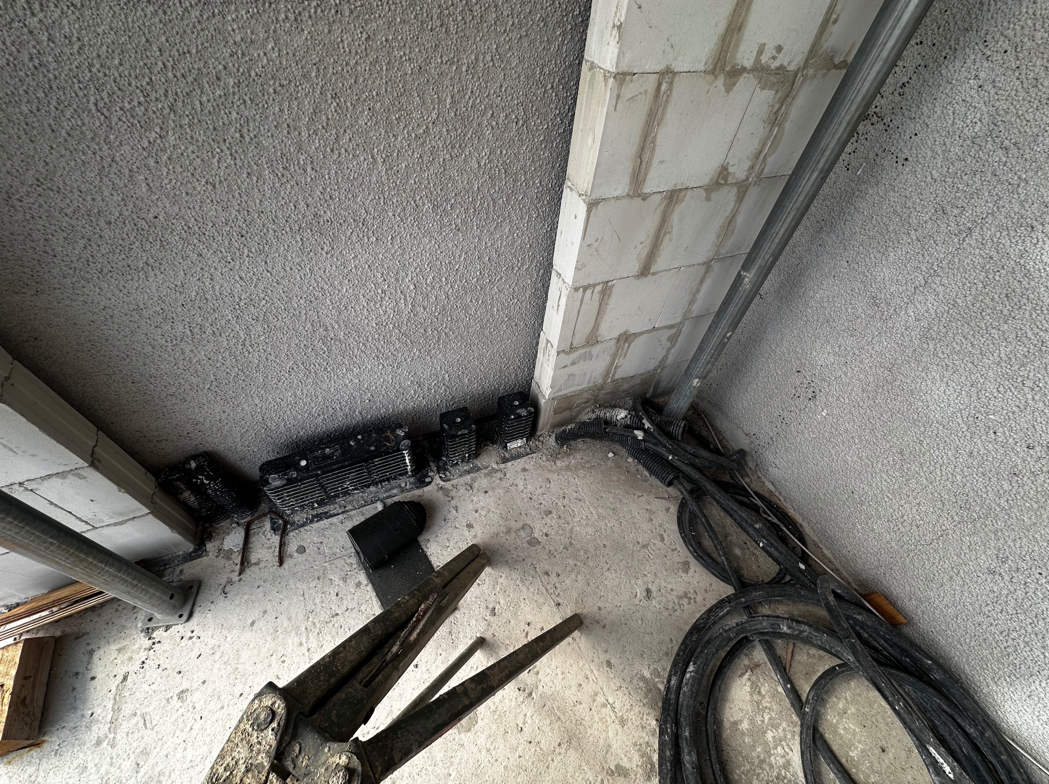 Niezwykłe ujęcie z dołu: kable elektryczne, narzędzia i elementy instalacji w surowym wnętrzu, ukazujące etap prac instalacyjnych. Widoczne detale betonu i cegieł.