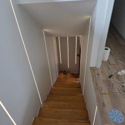 PACH-BUD Rafał Pach - Schody drewniane z oświetleniem LED w ścianach, widok z góry. Widoczne narzędzia i materiały wykończeniowe, co sugeruje etap prac wykończeniowych.
