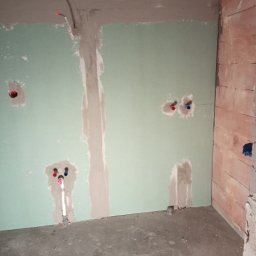 DB-est - Ściana z płyt gipsowo-kartonowych po szpachlowaniu, widoczne instalacje wodne i elektryczne. Surowy stan wykończenia wnętrza, przygotowanie do dalszych prac.