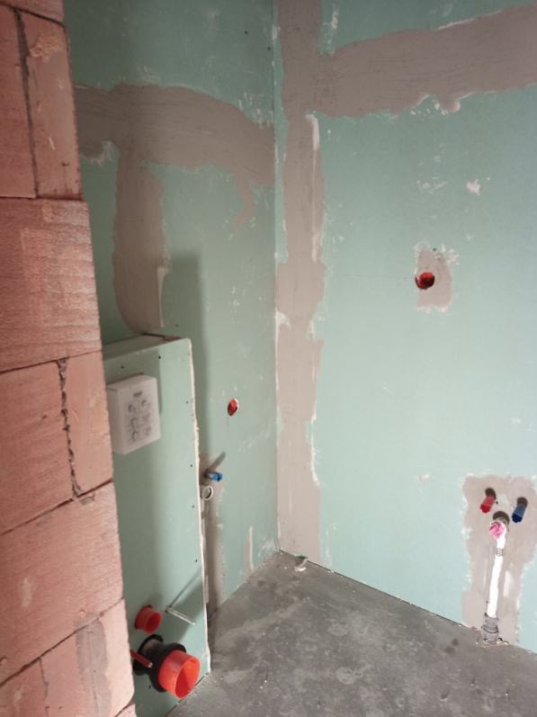 Wnętrze w trakcie prac wykończeniowych: ściany z płyt gipsowo-kartonowych z widocznymi łączeniami, instalacja wodno-kanalizacyjna, fragment ściany z cegły.