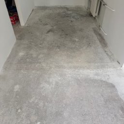 Rafal Kubiak - Przygotowana, szara, surowa podłoga w pustym pomieszczeniu z grzejnikiem, gotowa do dalszych prac wykończeniowych. Widoczne ślady po szlifowaniu.