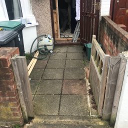 Rafal Kubiak - Remont wejścia do domu: malowanie drzwi wejściowych, widoczny odkurzacz przemysłowy, drabina i fragment drewnianego ogrodzenia. Prace w toku.