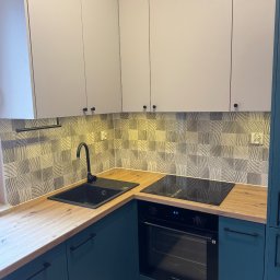 Nowoczesna kuchnia w Krakowie: turkusowe szafki dolne, jasne górne, drewniany blat i wzorzyste płytki. Czarny zlew i płyta indukcyjna. Stylowe wykończenie.