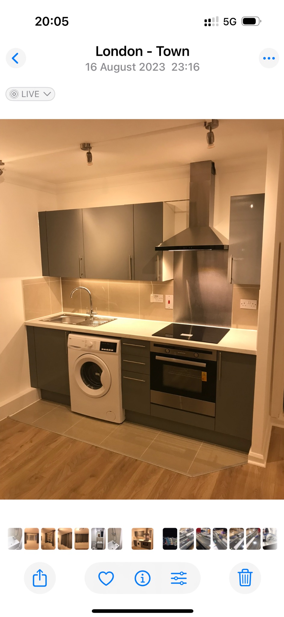 Nowoczesna kuchnia w szarościach z drewnianą podłogą. Zabudowa kuchenna z pralką, piekarnikiem i płytą indukcyjną. Stalowy okap i oświetlenie podszafkowe.