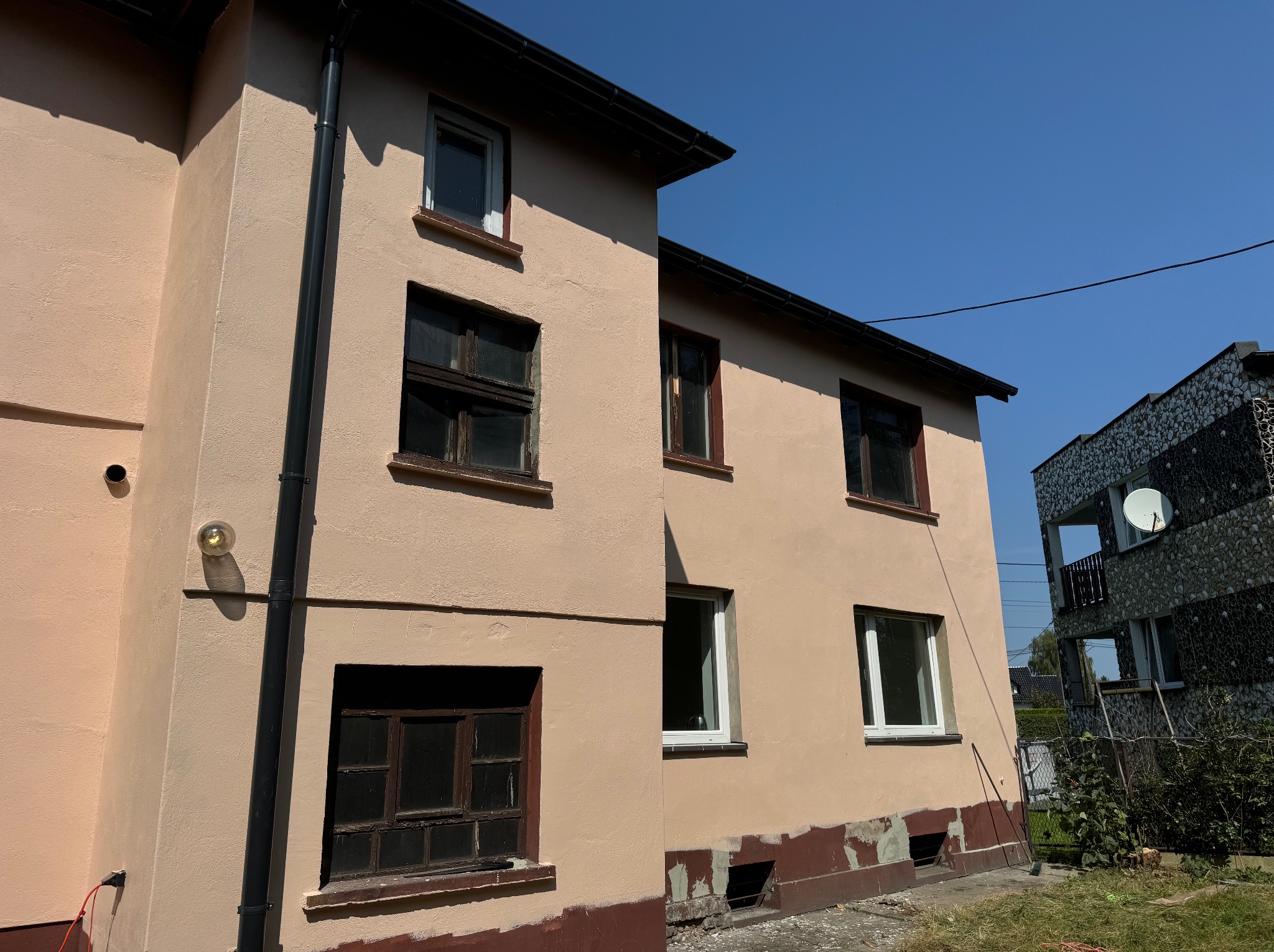 Elewacja budynku po malowaniu, z widocznymi fragmentami starej farby u dołu. Nowe okna wstawione, stare okna jeszcze nie wymienione. Słoneczny dzień.