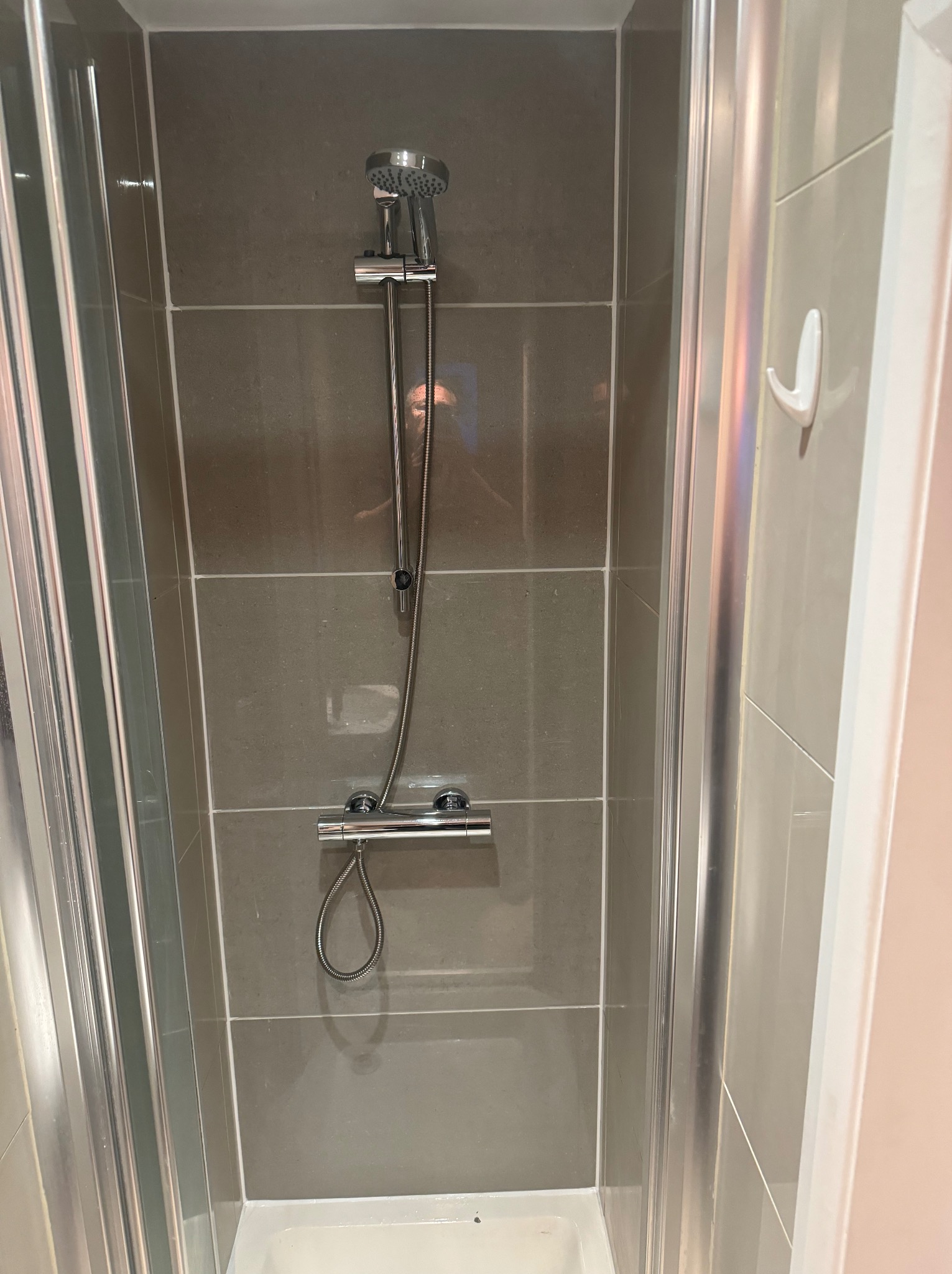 Kabina prysznicowa z szarymi płytkami, chromowaną armaturą i uchwytem na ścianie. Widok z bliska, prezentujący detale wykończenia.