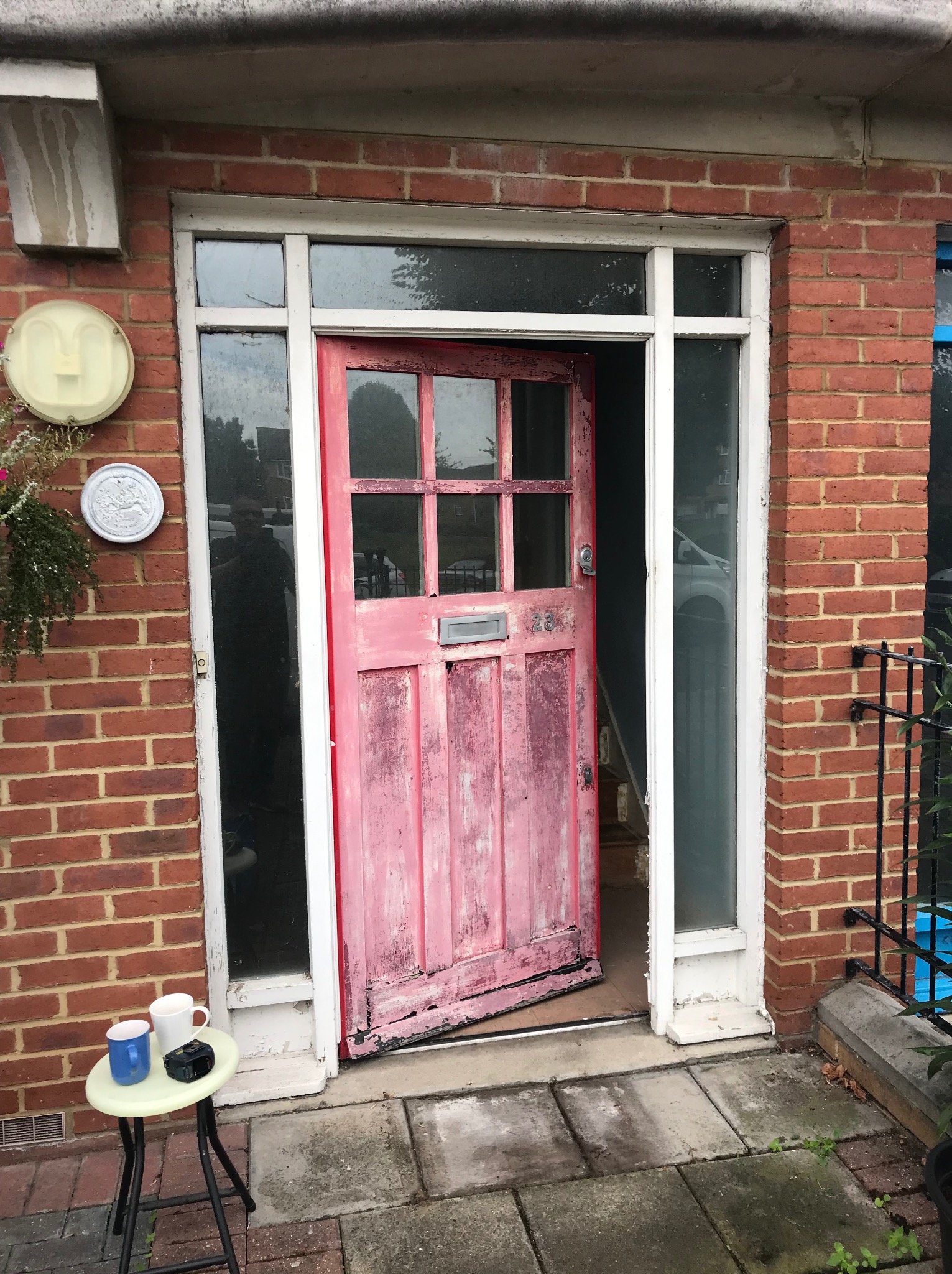Otwarta, stara, różowa, drewniana brama wejściowa z szybami, z widocznymi śladami zużycia i łuszczącej się farby, wkomponowana w ceglaną fasadę budynku.