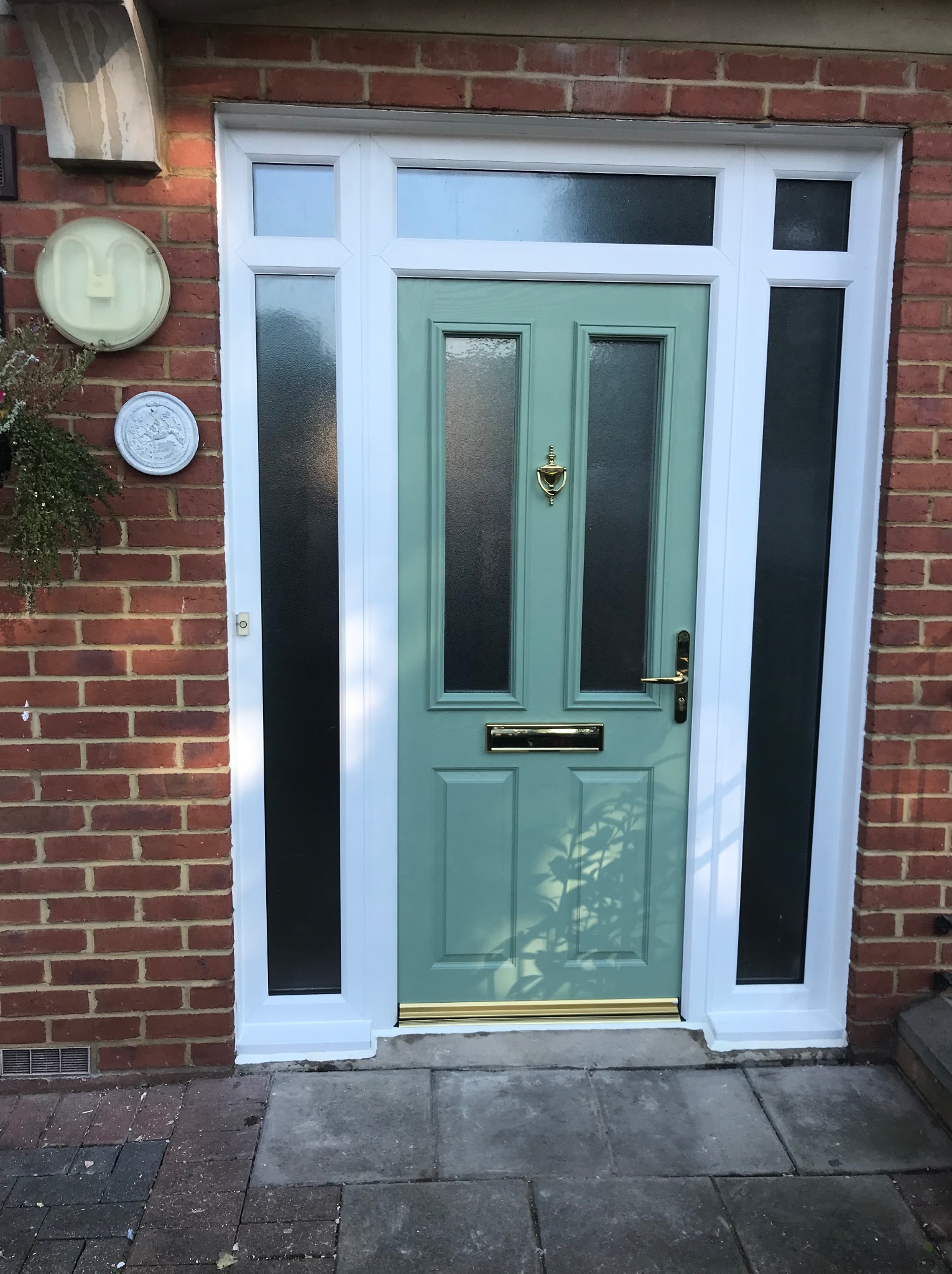 Turkusowe drzwi wejściowe z szybami i złotymi detalami, osadzone w białej ramie, na tle ceglanej ściany. Widoczne elementy dekoracyjne na elewacji.