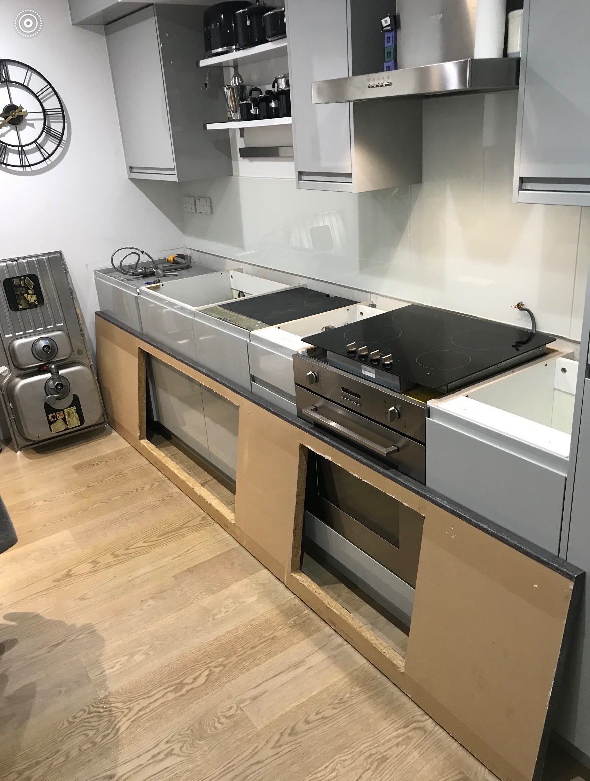 Montaż nowoczesnej kuchni: szare szafki, płyta indukcyjna i piekarnik w zabudowie. Widoczny zdemontowany zlew i elementy konstrukcyjne szafek.