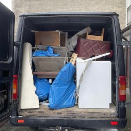 WolnaPrzestrzeńUtylizacja - Czarny van z otwartymi drzwiami bagażnika, wypełniony meblami, sprzętem AGD i workami na śmieci. Widoczne elementy wyposażenia wnętrz i sprzęt gotowy do transportu.