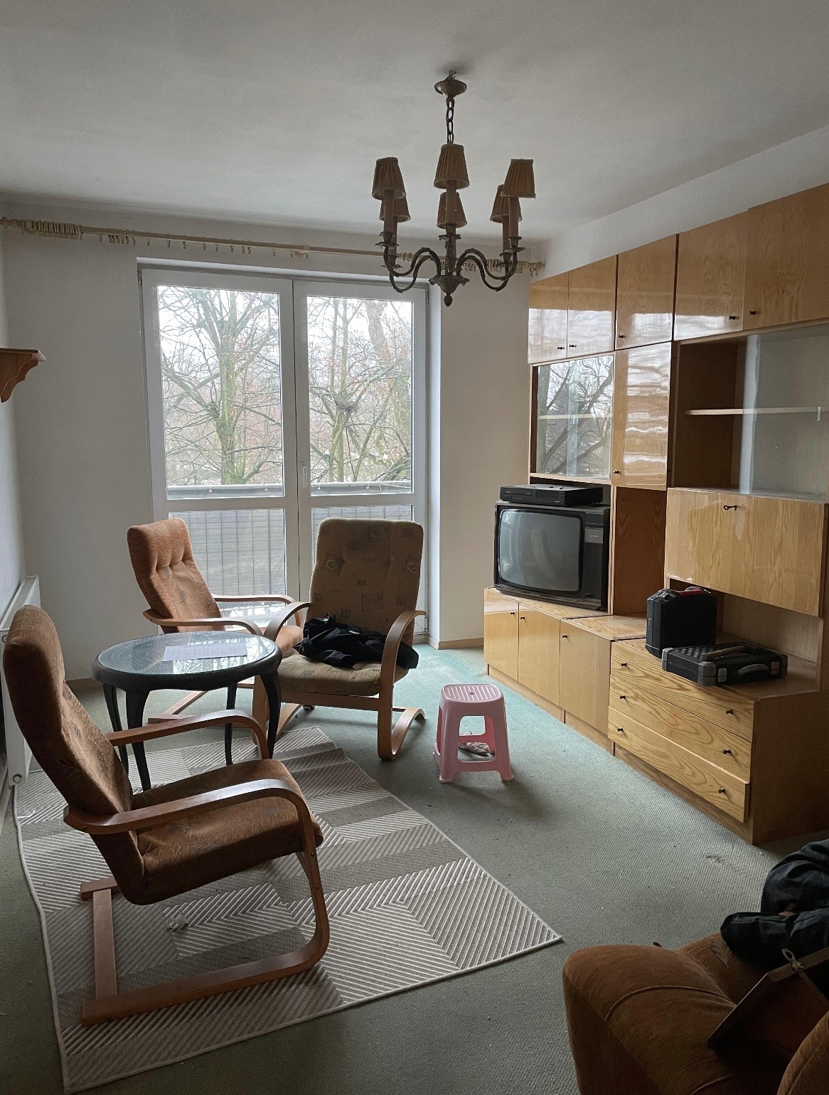 Pokój z lat 80. z meblościanką, telewizorem kineskopowym i brązowymi fotelami. Widoczne ślady użytkowania, sugerujące potrzebę odświeżenia lub opróżnienia.