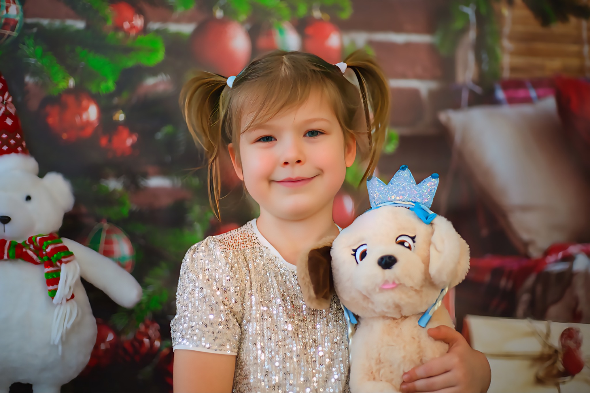 Uśmiechnięta dziewczynka w cekinowej bluzce, z pluszowym pieskiem w koronie na tle świątecznej dekoracji z choinką i prezentami. Portret w ciepłych barwach.
