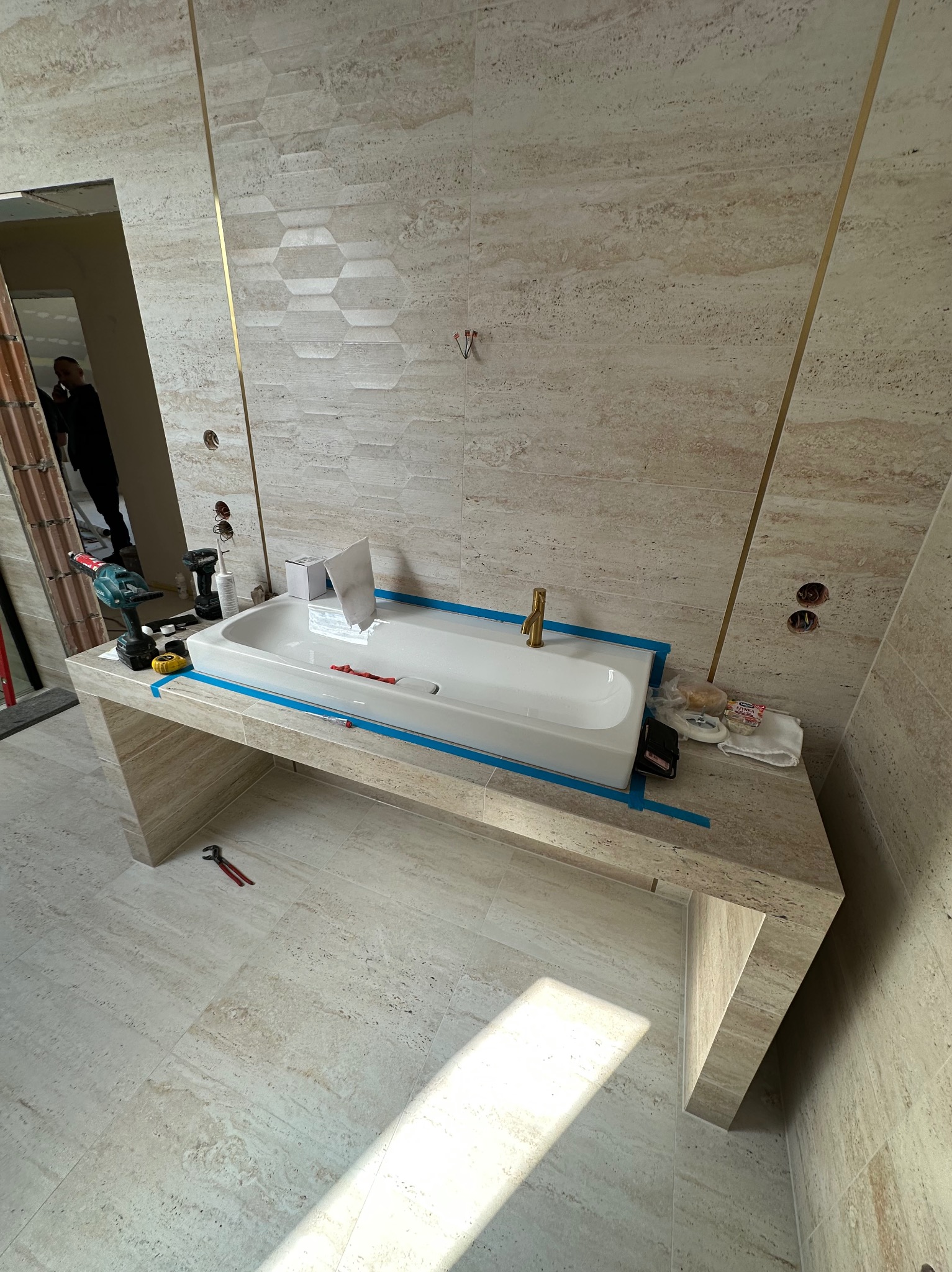 Montaż umywalki nablatowej w łazience wykończonej trawertynem z elementami złota. Widoczne narzędzia i materiały montażowe. Ujęcie z góry, w trakcie prac.