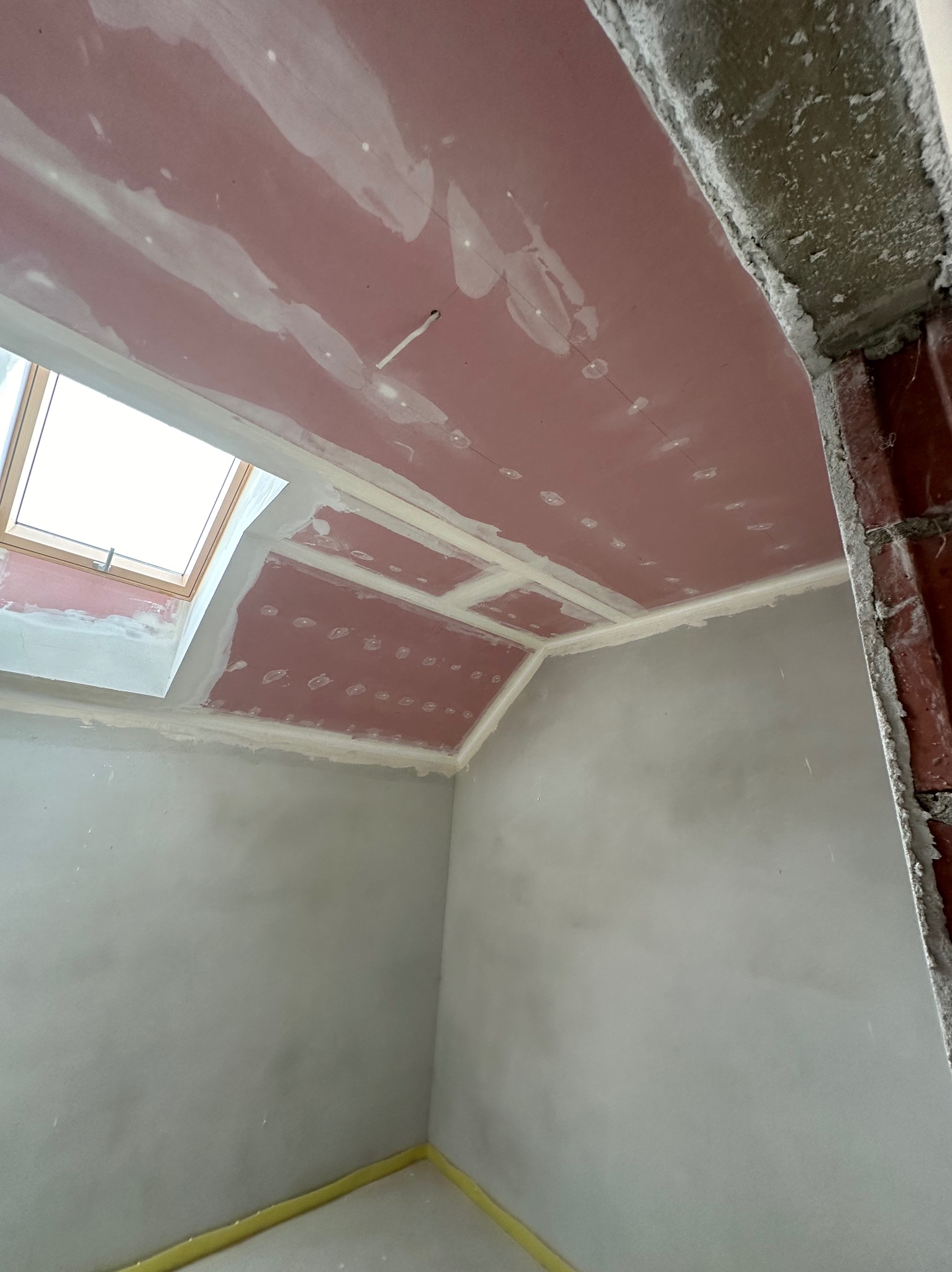 Płyty karton-gips na suficie poddasza ze świetlikiem, przygotowane do szpachlowania. Widoczne łączenia i ślady po wkrętach. Ściany wstępnie wygładzone.