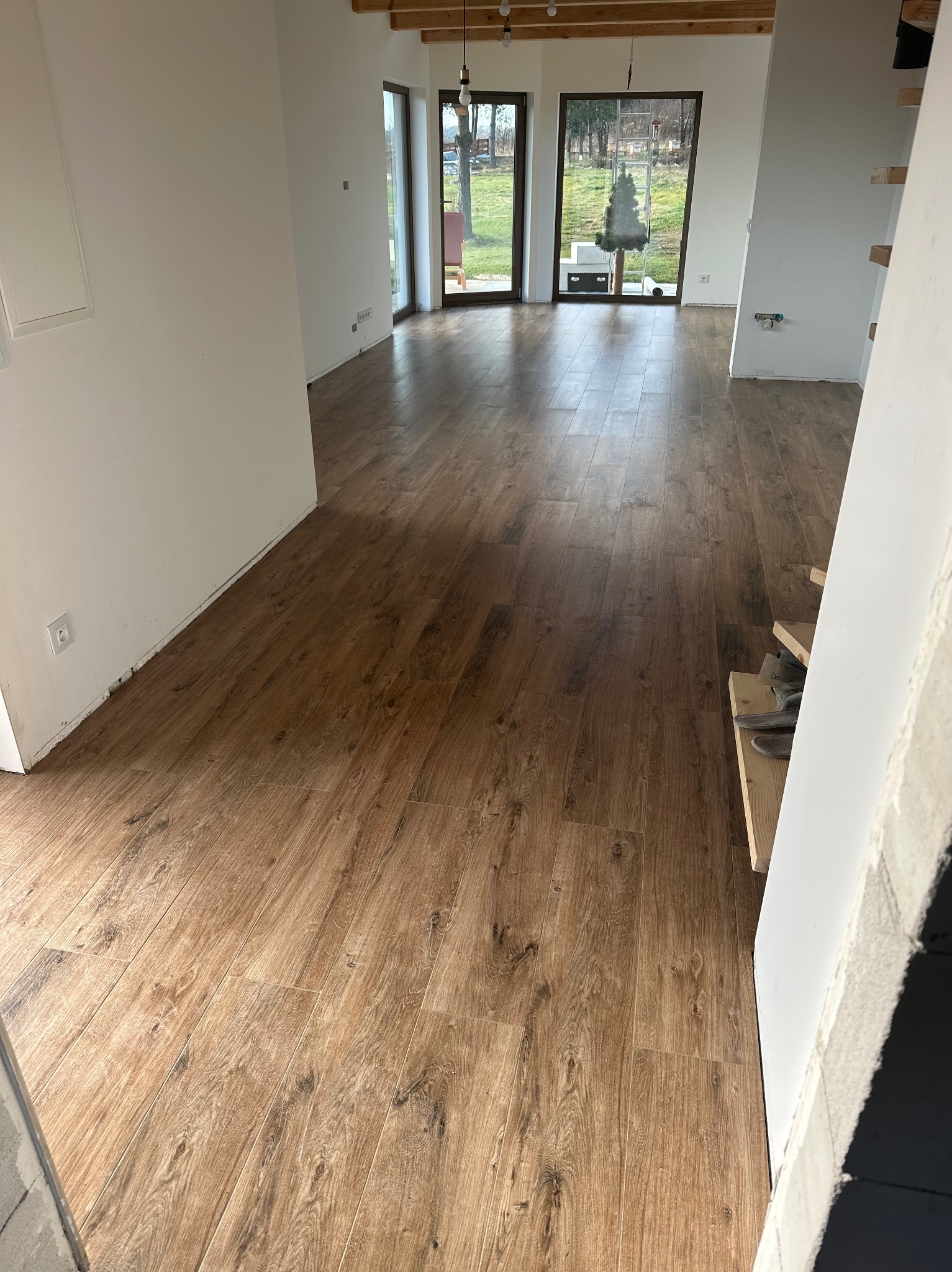 Ukończona podłoga z paneli drewnopodobnych w jasnym, przestronnym wnętrzu z dużymi oknami i widoczną konstrukcją drewnianą sufitu. Widoczne fragmenty schodów.