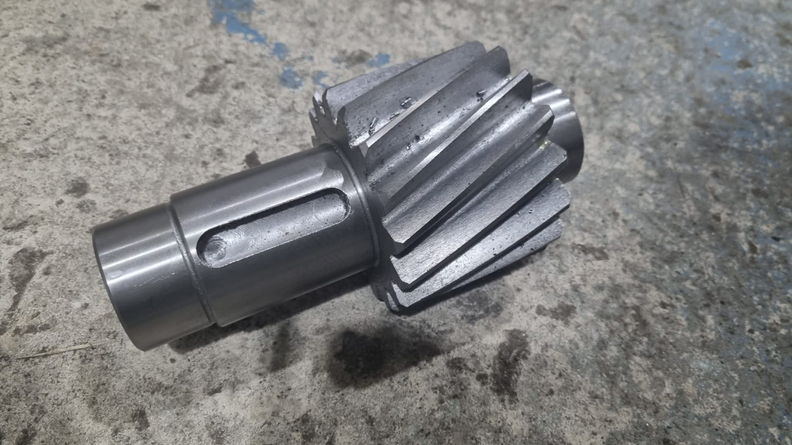 Metalowa przekładnia z zębami śrubowymi, widoczne ślady obróbki, leżąca na szarej, betonowej powierzchni. Precyzyjna obróbka metalu.