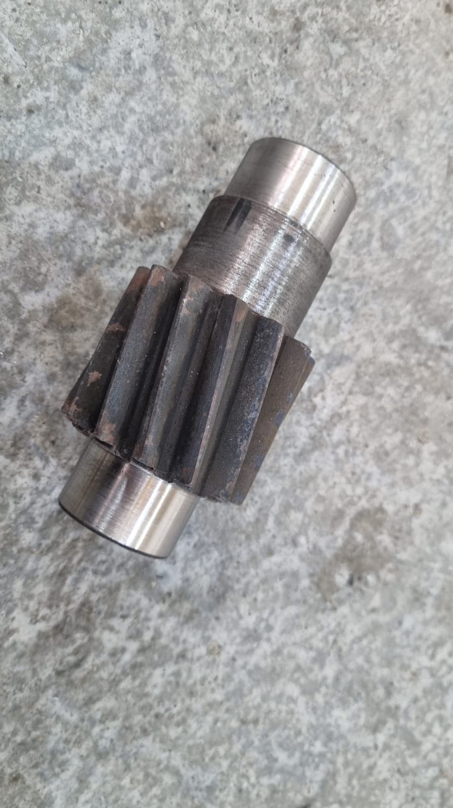 Metalowa zębatka z widocznymi śladami użytkowania, leżąca na szarej, chropowatej powierzchni. Detal obróbki metalu, prezentujący precyzję wykonania i zużycie.