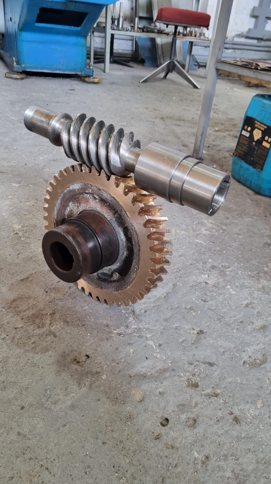 Precyzyjnie wykonana przekładnia ślimakowa z brązu i stali na szarym tle warsztatowym. Widoczne ślady obróbki i zużycia, podkreślające funkcjonalność elementu.