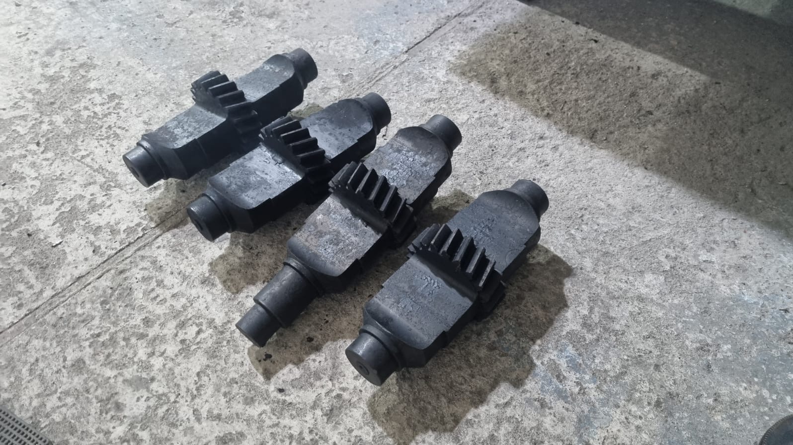 Cztery czarne, metalowe elementy z zębatymi krawędziami leżą na szarej, betonowej powierzchni. Elementy są ułożone ukośnie, jeden za drugim, w bliskiej odległości.