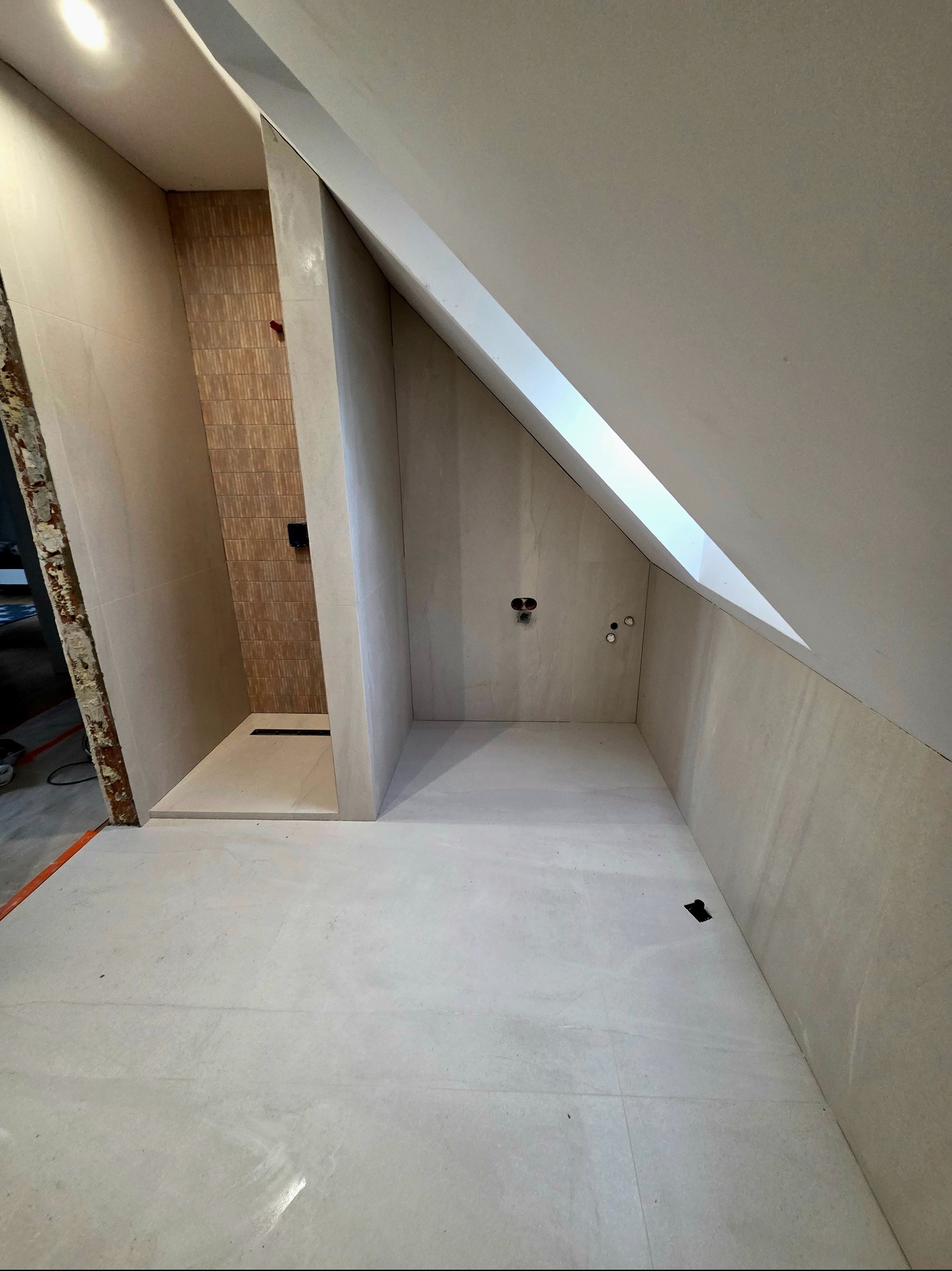 Wykończona łazienka na poddaszu ze skośnym sufitem, beżowe płytki na ścianach i podłodze, kabina prysznicowa z odpływem liniowym, przygotowane punkty elektryczne.