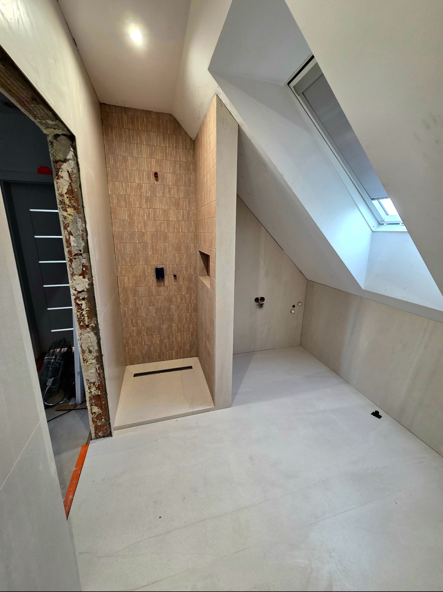 Wykończona łazienka na poddaszu w Mszanie Dolnej. Beżowe płytki w kabinie prysznicowej, jasne płytki na podłodze i ścianach. Okno dachowe w skosie.