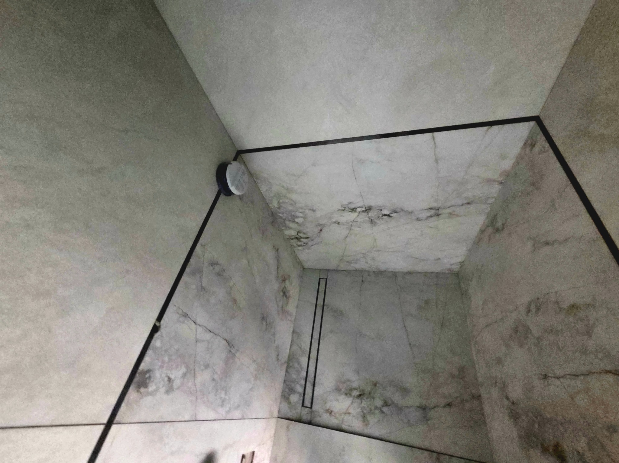 Wykończona kabina prysznicowa z odpływem liniowym i marmurowymi płytkami na ścianach i podłodze. Widok z góry, podkreślający precyzję ułożenia płytek i estetykę wykończenia.