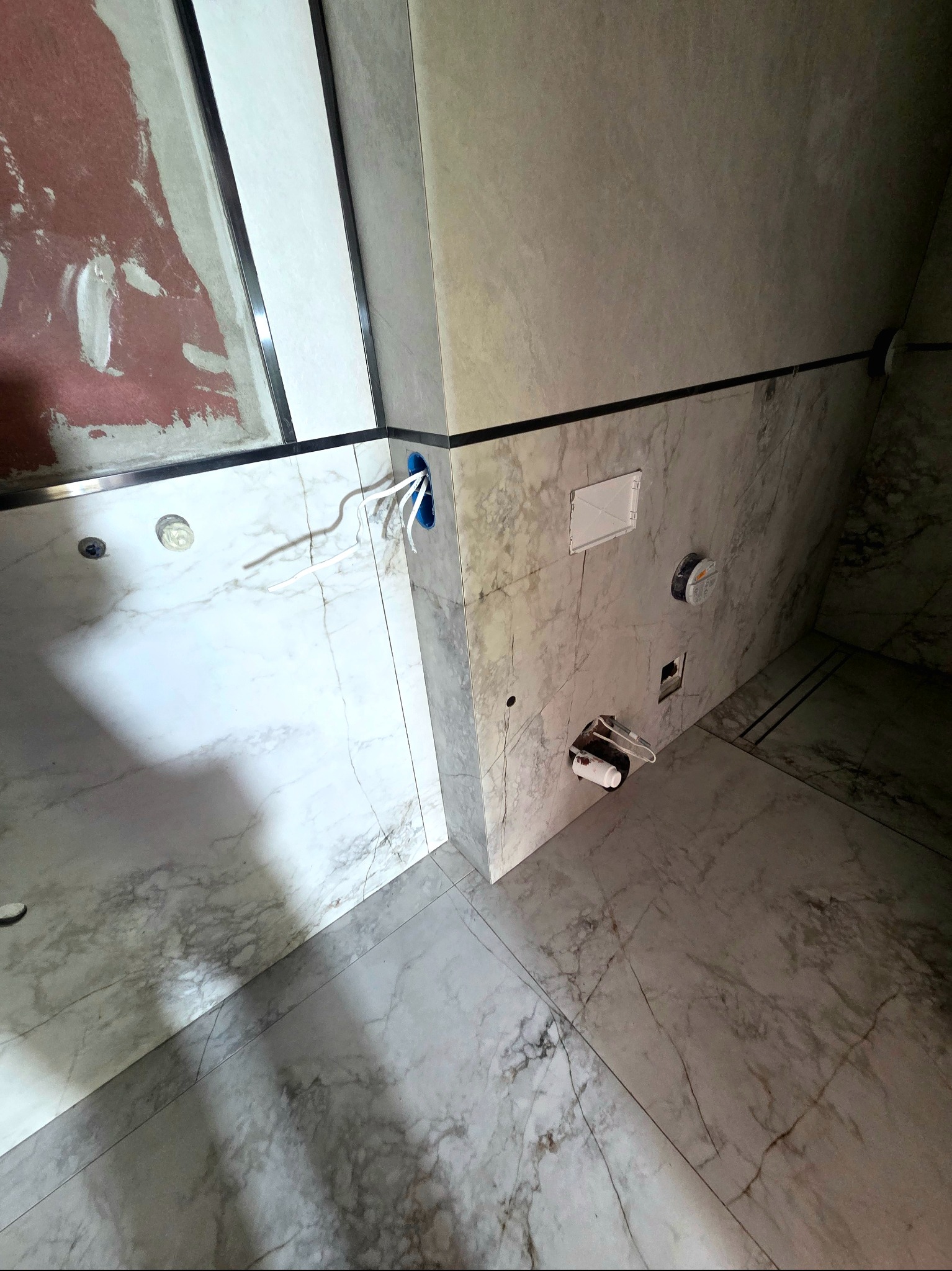 Łazienka w trakcie wykańczania: marmurowe płytki, wystające przewody elektryczne, elementy instalacji sanitarnej. Widok z góry, ukośne ujęcie.