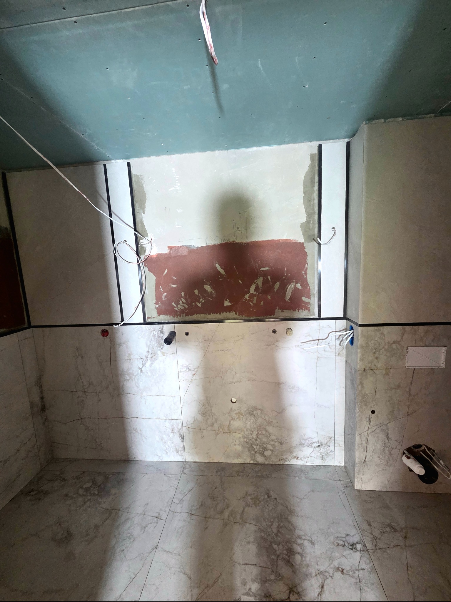 Wnętrze łazienki w trakcie prac wykończeniowych: położone marmurowe płytki na podłodze i ścianach do połowy wysokości, widoczne instalacje i surowy sufit.