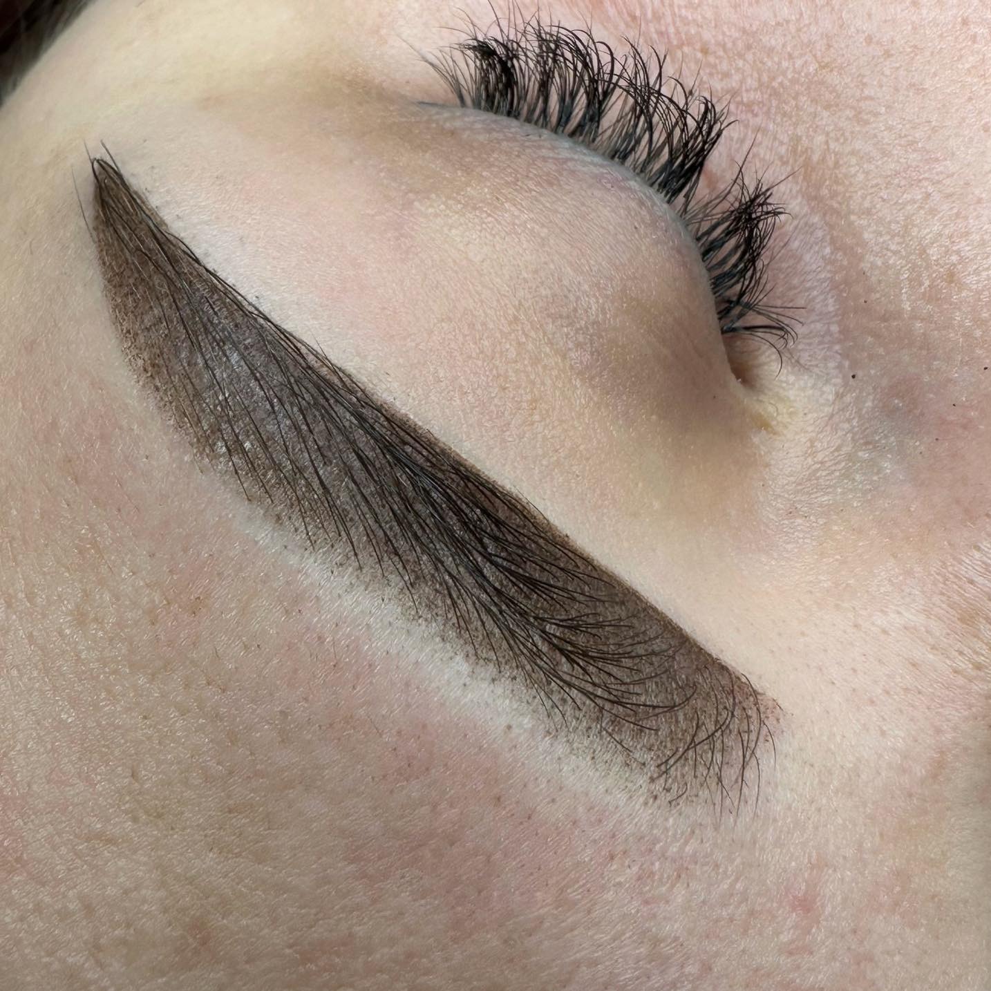 Makro zbliżenie na oko z idealnie wystylizowaną brwią metodą microbladingu. Widoczne pojedyncze włoski i naturalny efekt. Długie rzęsy dodają uroku.