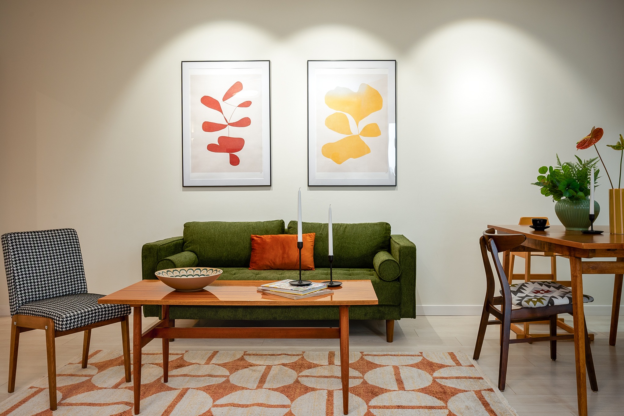Salon w stylu retro z zieloną sofą, drewnianym stolikiem kawowym i dywanem w geometryczne wzory. Na ścianie wiszą abstrakcyjne obrazy w czarnych ramach.