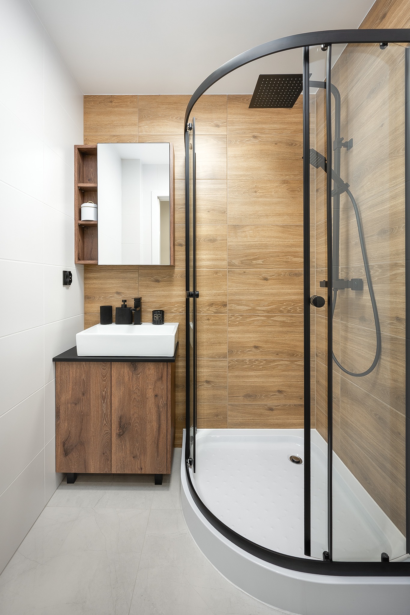 Nowoczesna łazienka z kabiną prysznicową typu walk-in z czarnymi profilami, drewnopodobnymi płytkami i szafką z umywalką nablatową. Minimalistyczny design.
