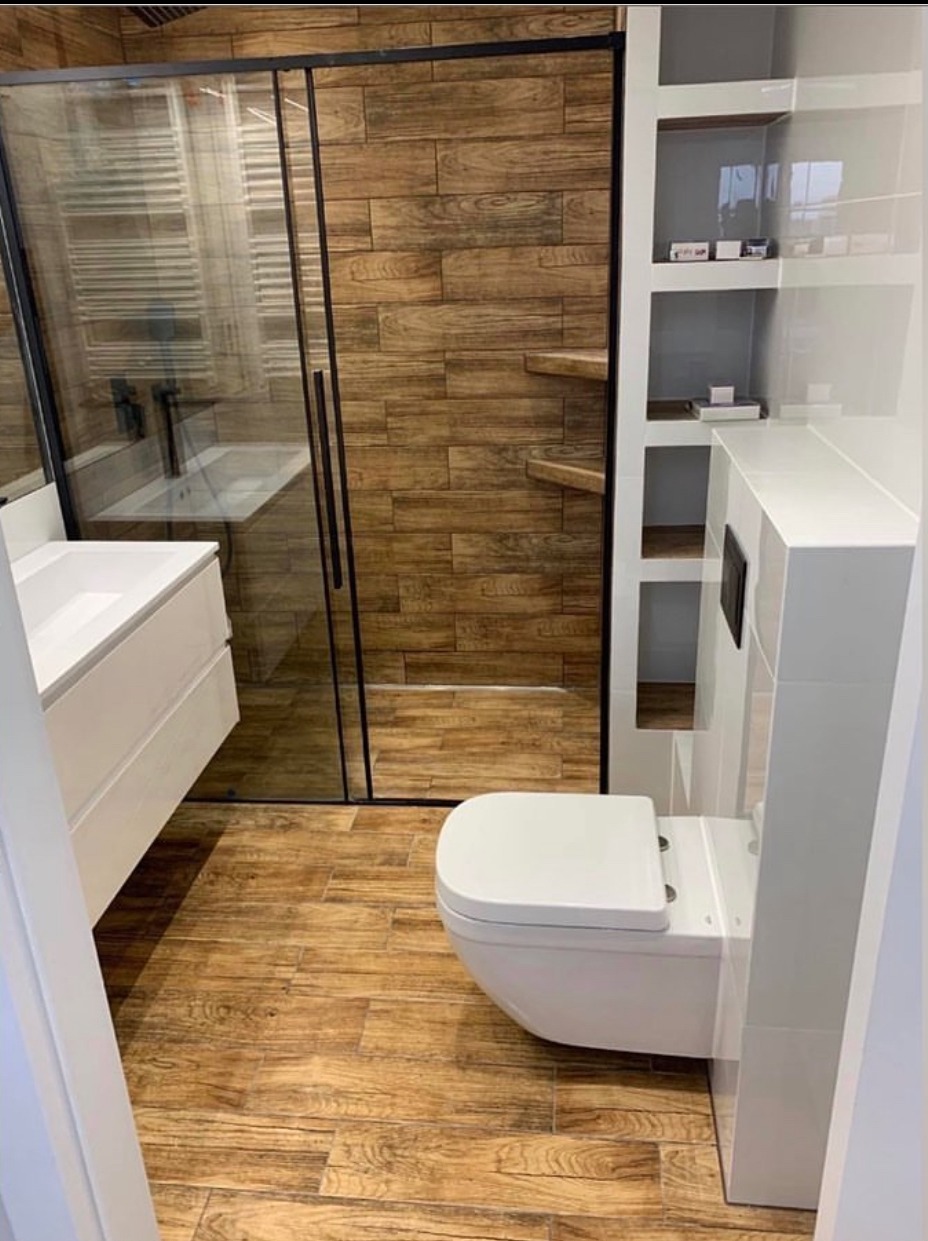 Nowoczesna łazienka z kabiną prysznicową typu walk-in, drewnopodobnymi płytkami i podwieszaną toaletą. Minimalistyczny design z akcentami drewna.