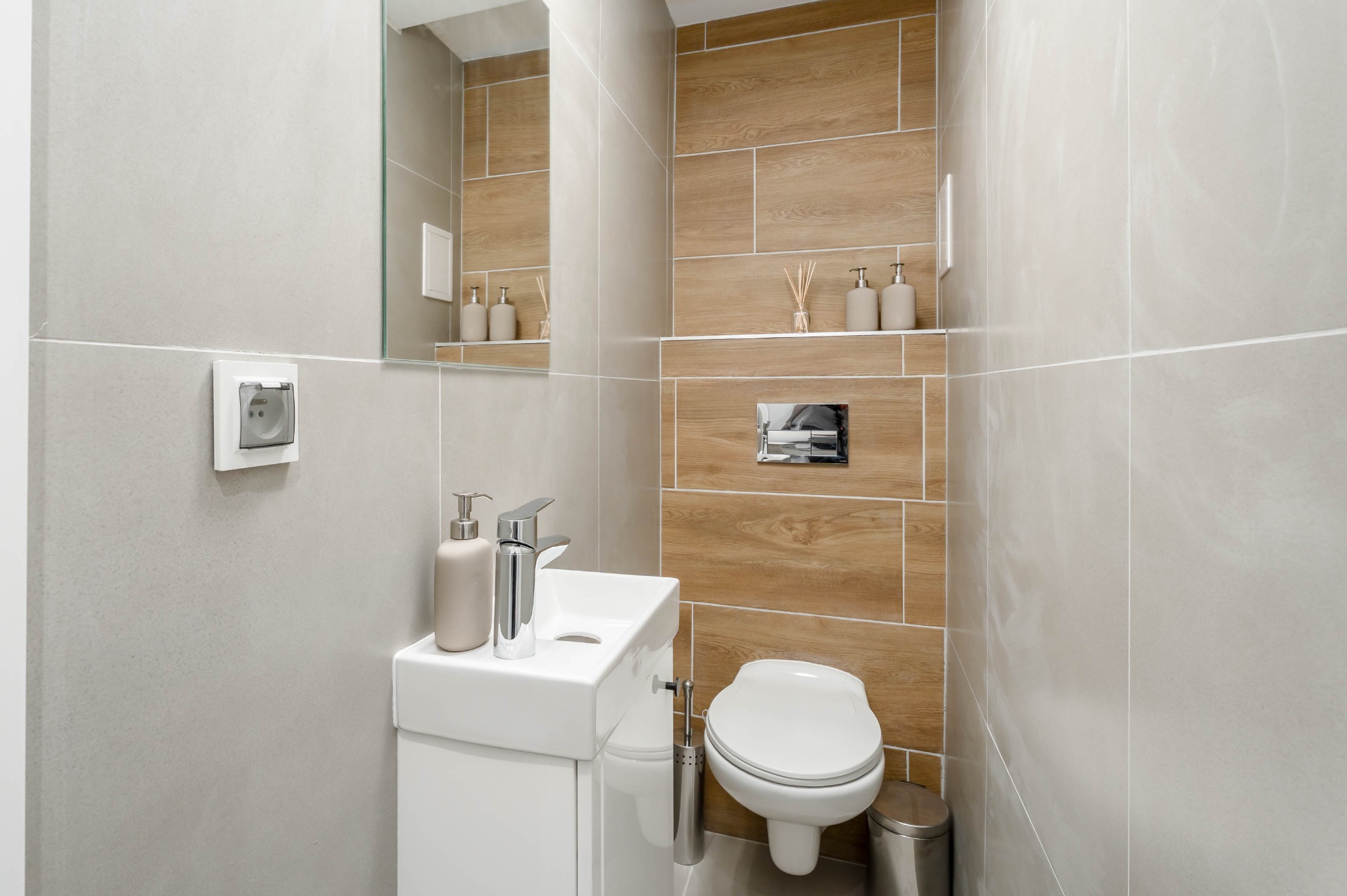 Nowoczesna łazienka z drewnopodobnymi i szarymi płytkami. Umywalka nablatowa, wisząca toaleta i minimalistyczne dodatki tworzą spójną całość.