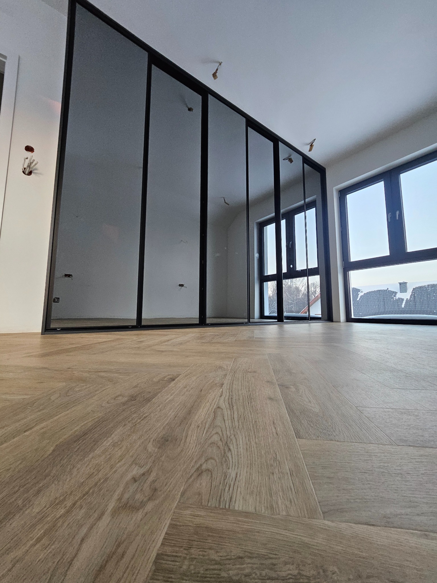 Nowoczesna szafa wnękowa z czarnymi ramami i lustrzanymi drzwiami, widok z dołu na parkiet w jasnym wnętrzu. Minimalistyczny design, duże okna.