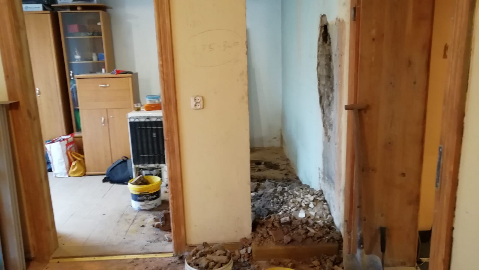 Demontaż ściany działowej w mieszkaniu: gruz na podłodze, odsłonięta instalacja elektryczna, widoczne ślady po kuciu w ścianie, przygotowania do dalszych prac.