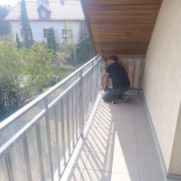 Adam walczy WELLSPAW - Montaż balustrady balkonowej z metalu przez montera na balkonie z widokiem na zieleń. Widoczne narzędzia i elementy konstrukcyjne.