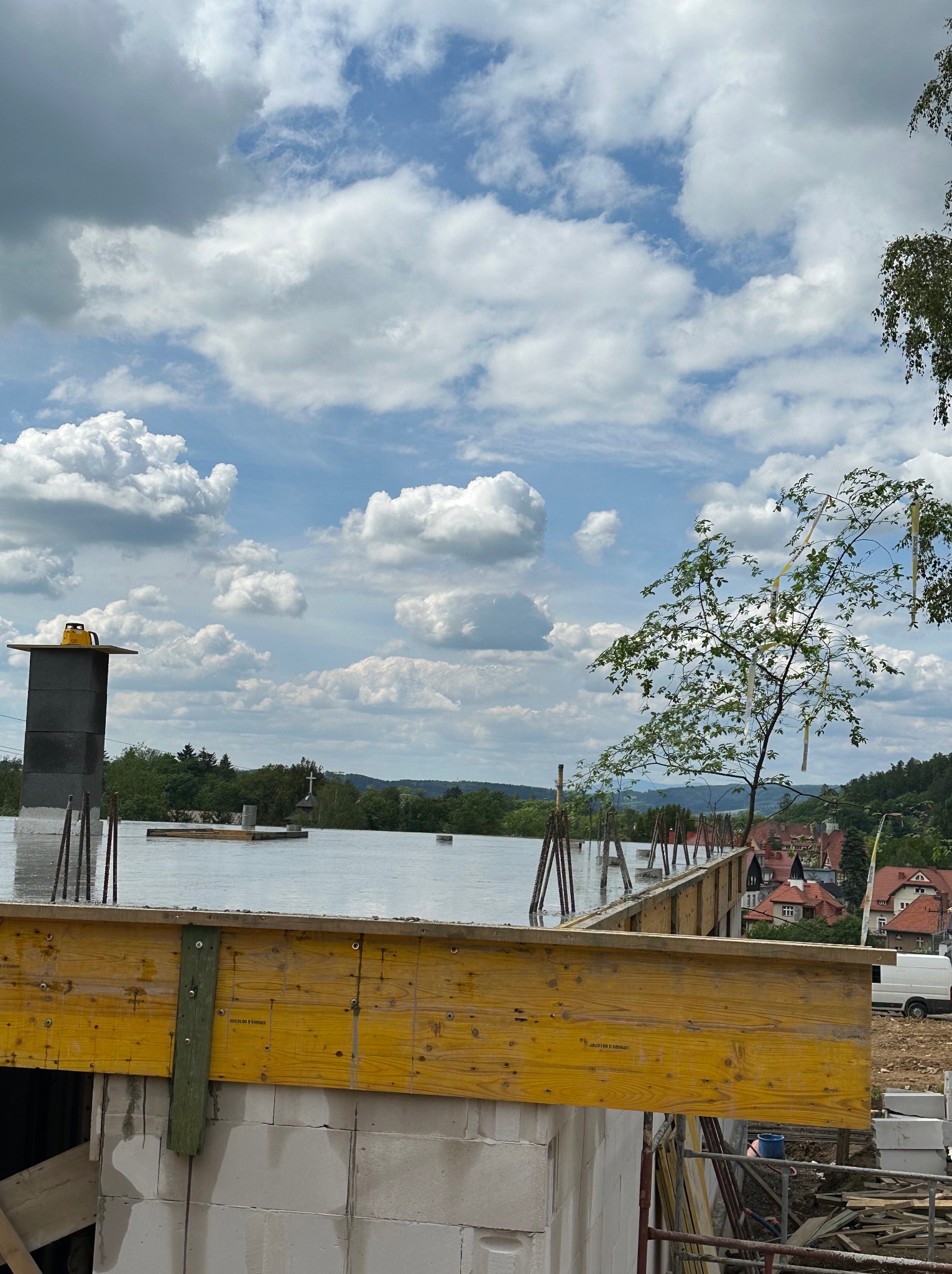 Wylany strop na budynku w trakcie budowy, widoczne szalunki i zbrojenie. W tle zabudowa jednorodzinna i błękitne niebo z chmurami.