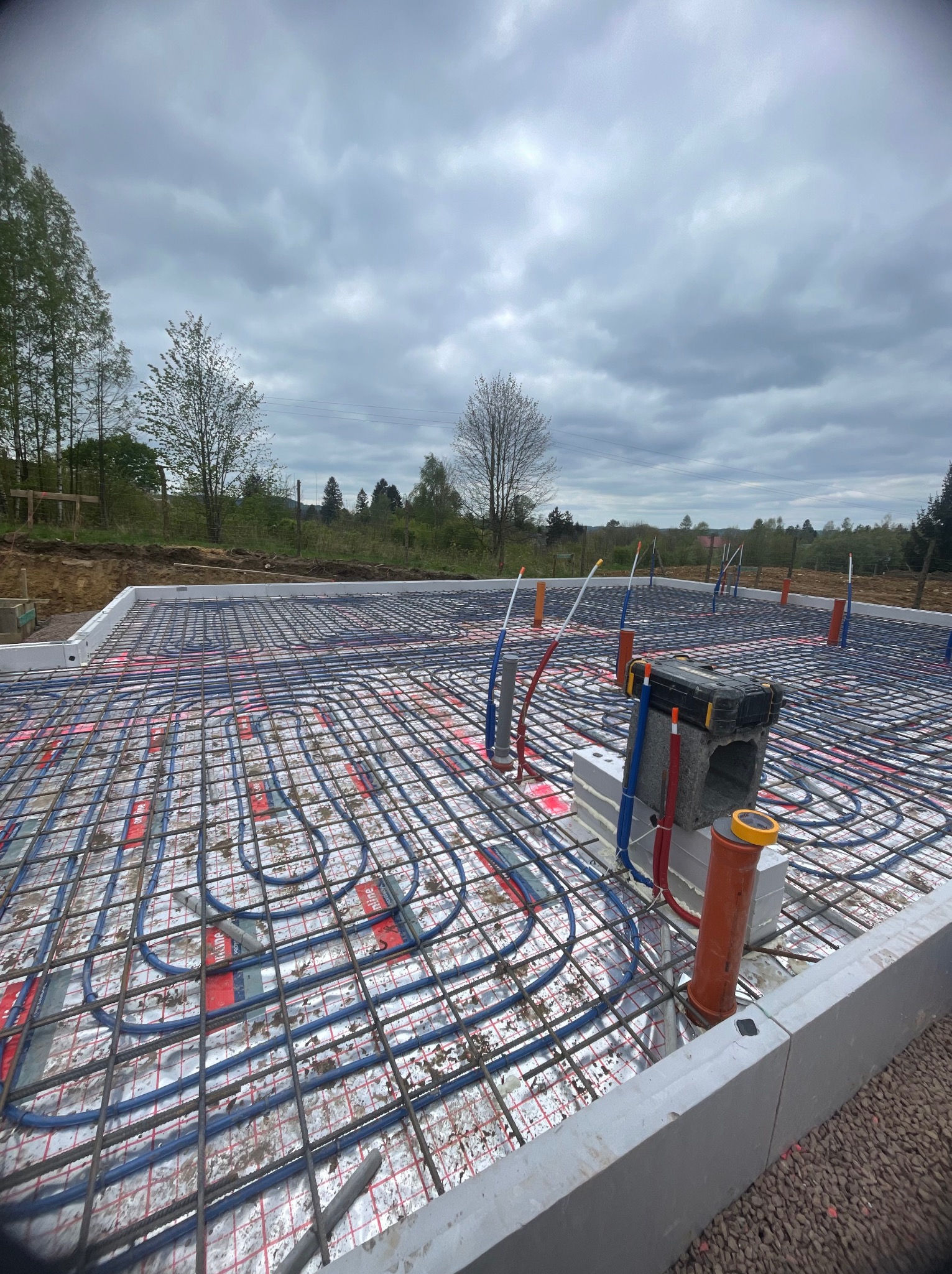 Instalacja ogrzewania podłogowego w fundamencie domu jednorodzinnego, widok z góry na rozłożone rury grzewcze i zbrojenie na izolacji, przygotowane do zalania betonem.
