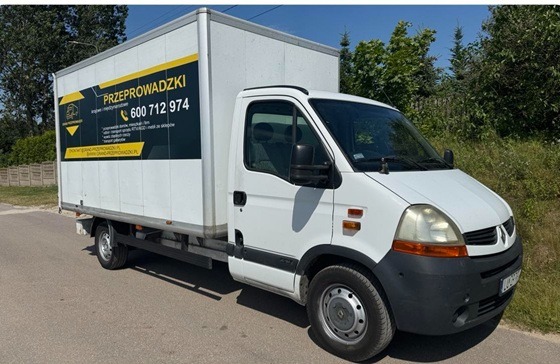 Biały samochód dostawczy Renault Master z reklamą firmy przeprowadzkowej, zaparkowany na ulicy w słoneczny dzień. Widoczny numer telefonu i adres strony internetowej.