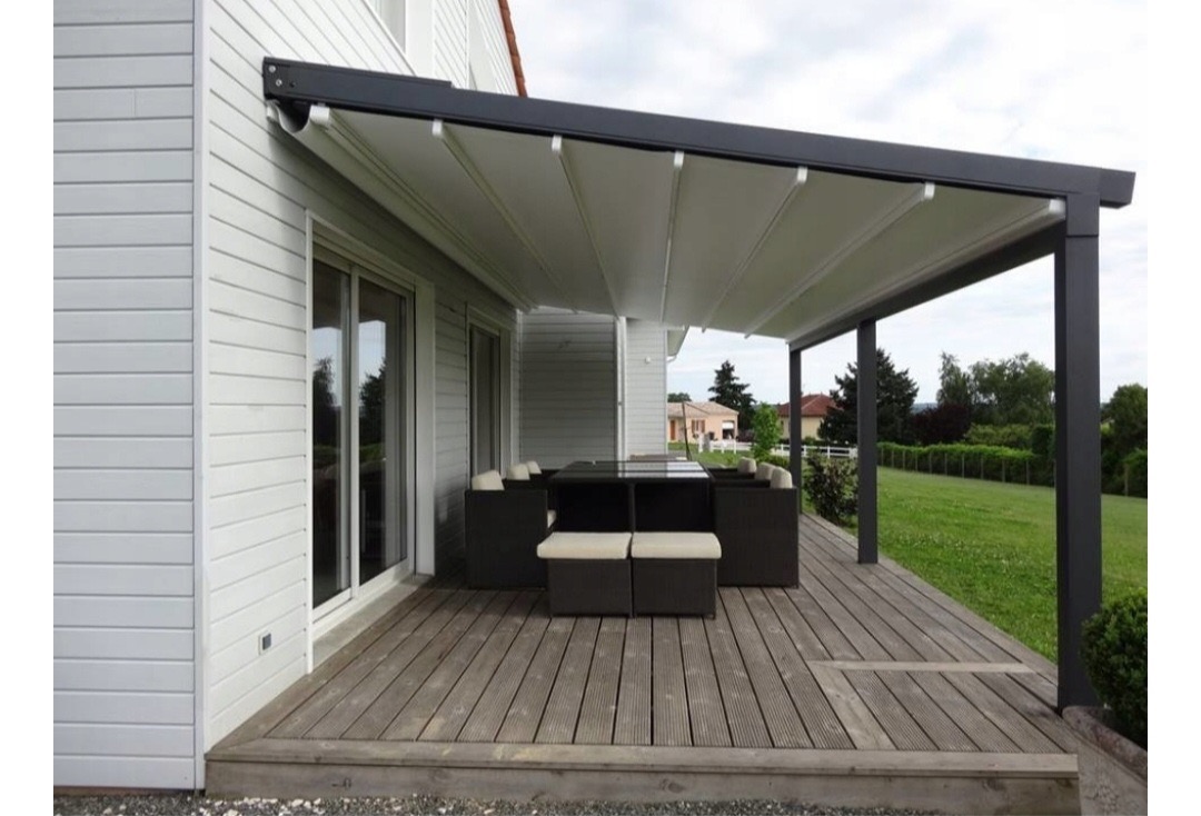 Nowoczesna pergola z rozsuwanym zadaszeniem, przylegająca do domu z drewnianą elewacją. Na tarasie drewnianym zestaw mebli ogrodowych.