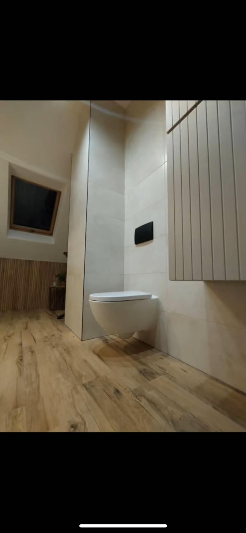 Nowoczesna toaleta podwieszana w jasnej łazience na poddaszu z drewnianą podłogą i grzejnikiem panelowym. Ukończone wykończenie wnętrza.