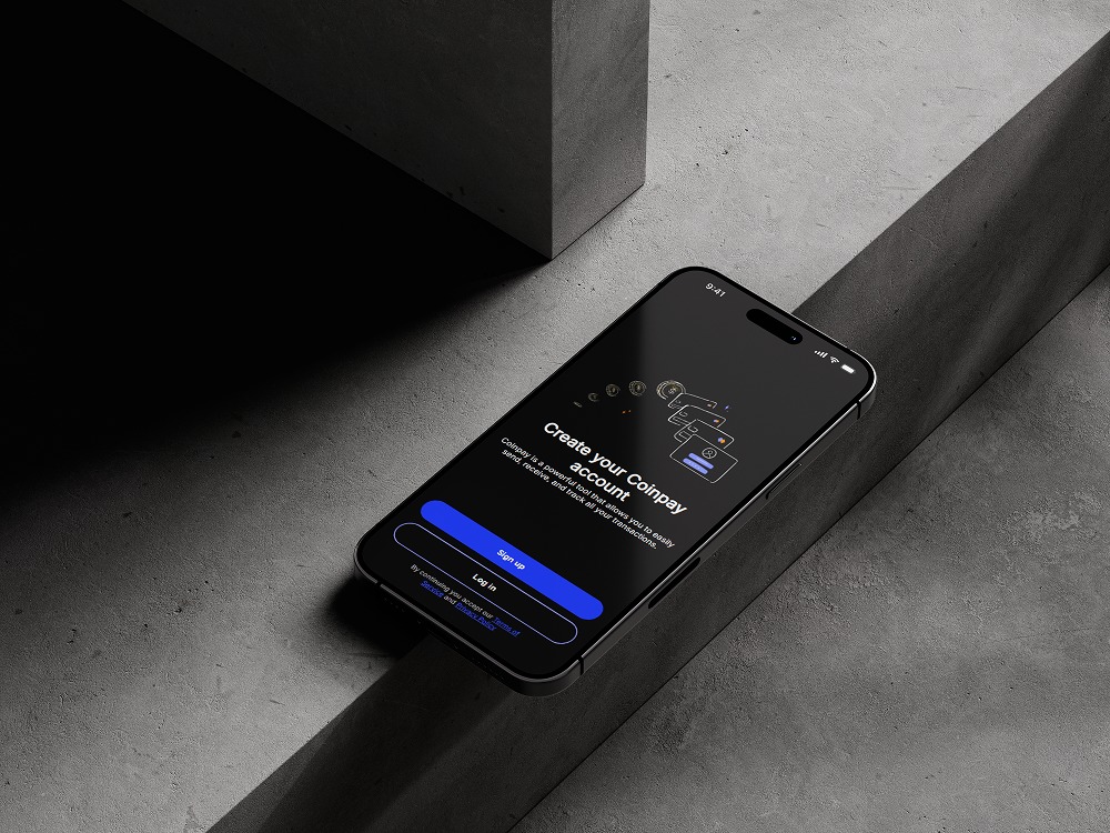 Ekran smartfona z interfejsem aplikacji Coinpay na tle betonowej powierzchni i cienia, prezentujący proces tworzenia konta z przyciskami 'Sign up' i 'Log in'.