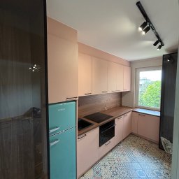 Pro-MB Stolarstwo - Nowoczesna kuchnia w kształcie L z pastelowymi szafkami, drewnianym blatem, czarnym sprzętem AGD i retro turkusową lodówką Amica. Wyróżniają ją wzorzyste płytki podłogowe i czarne oświetlenie szynowe.