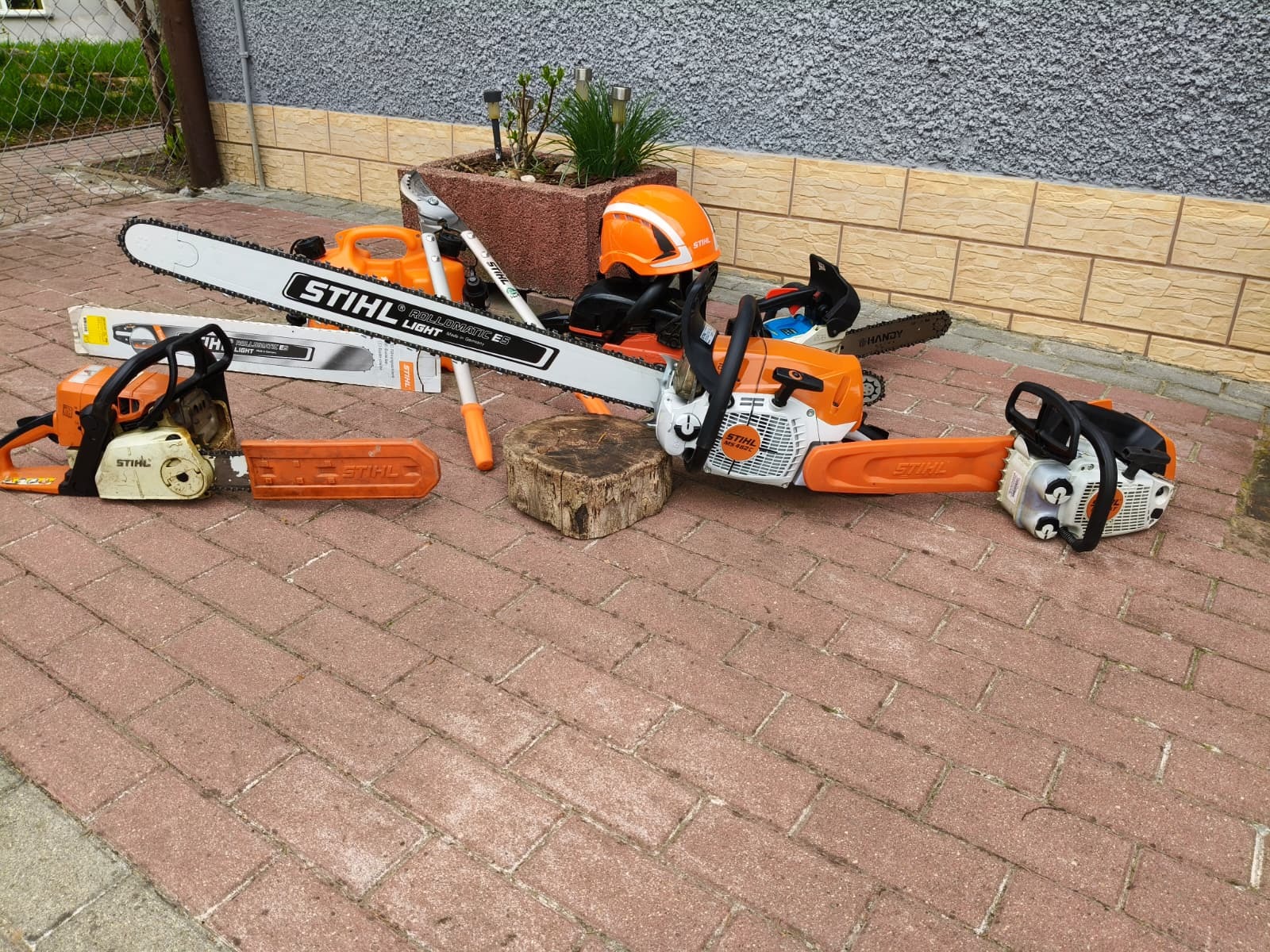 Zestaw narzędzi Stihl: piły łańcuchowe, sekator, kanister i kask na kostce brukowej. Prezentacja sprzętu do pielęgnacji zieleni.