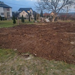 Olbud - Przygotowany teren pod budowę domu jednorodzinnego. W tle widoczne domy, drzewa i pozostałości po rozbiórce. Ziemia wyrównana, gotowa pod fundamenty.