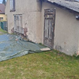 Olbud - Stary, częściowo zdemontowany budynek z uszkodzoną elewacją i dachem, zabezpieczony plandeką. Widoczne odsłonięte elementy konstrukcyjne i zniszczone okna.